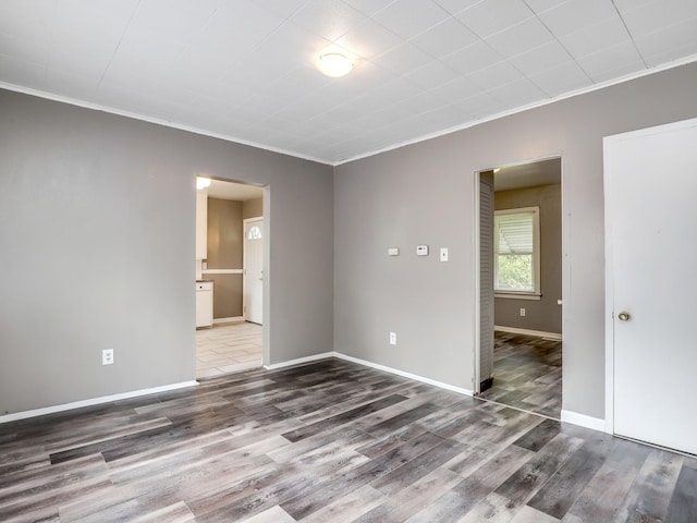 empty room featuring wood finished floors, crown molding, and baseboards