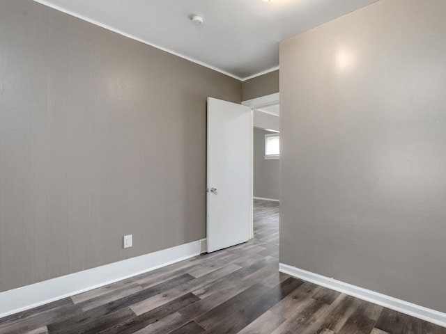 empty room with wood finished floors, baseboards, crown molding, and a smoke detector