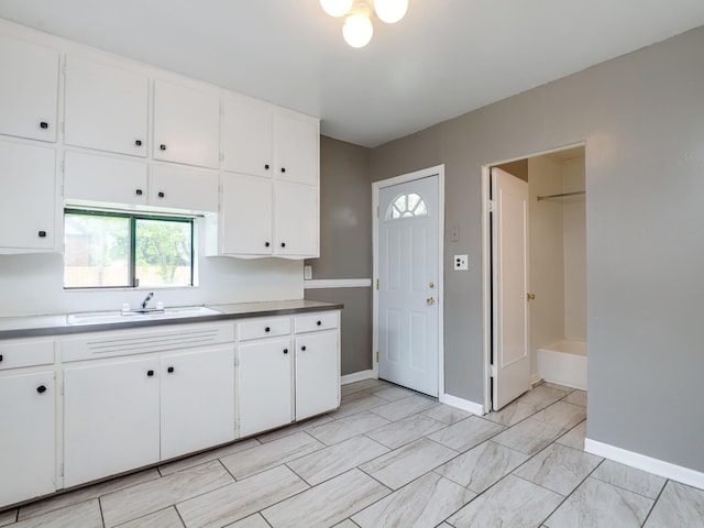 kitchen featuring white cabinets, baseboards, and a sink