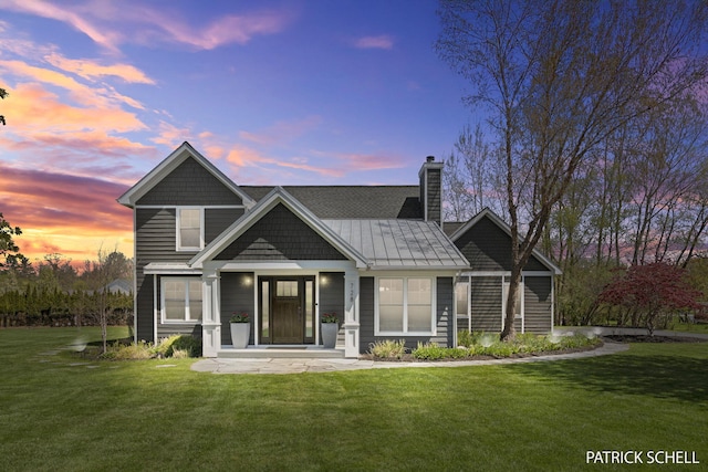 rear view of property featuring a lawn, a chimney, and a standing seam roof