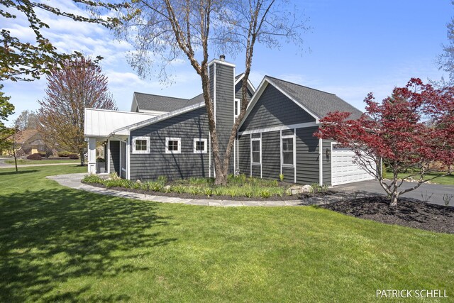 view of side of property featuring a chimney, a lawn, an attached garage, and concrete driveway