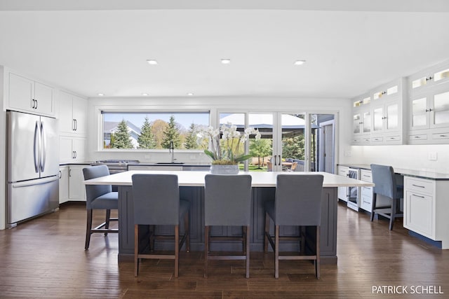 kitchen with stainless steel fridge, a sink, a breakfast bar, white cabinets, and recessed lighting