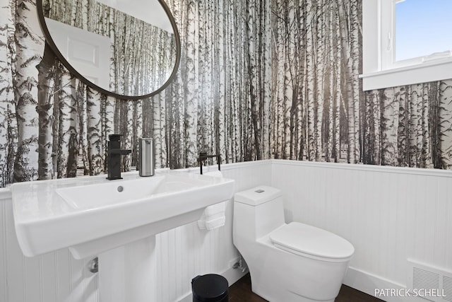 bathroom featuring a wainscoted wall, toilet, and wood finished floors