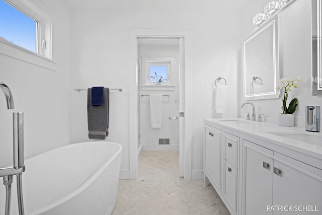 bathroom featuring healthy amount of natural light, a soaking tub, double vanity, and baseboards