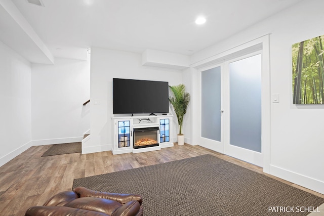 unfurnished living room featuring wood finished floors, stairs, recessed lighting, baseboards, and a glass covered fireplace