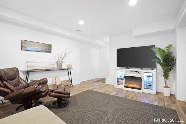 living area featuring wood finished floors, recessed lighting, a glass covered fireplace, and baseboards