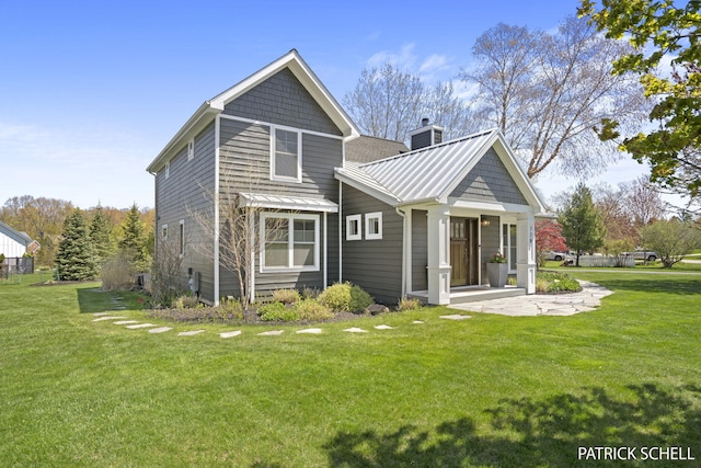 back of property with a standing seam roof, a yard, metal roof, and a chimney