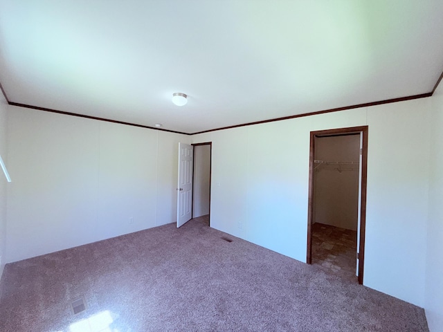 unfurnished bedroom with carpet, a spacious closet, crown molding, and a closet
