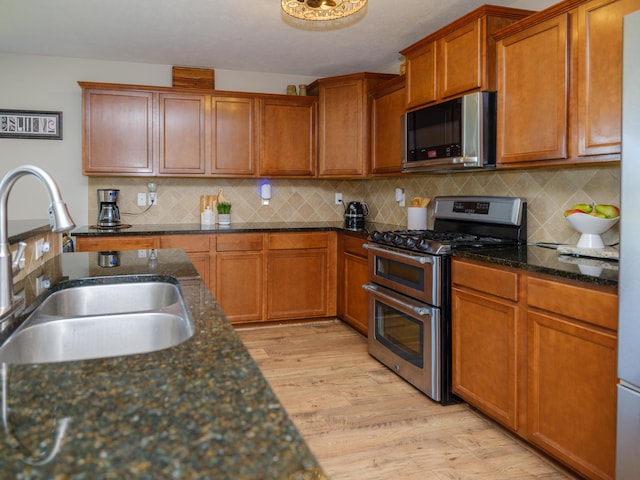 kitchen with stainless steel appliances, a sink, light wood-style floors, and decorative backsplash
