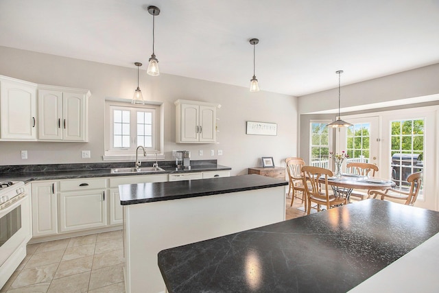 kitchen with a sink, dark countertops, white gas stove, white cabinetry, and pendant lighting