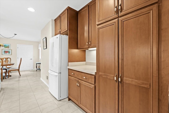 kitchen featuring freestanding refrigerator, brown cabinets, light countertops, light tile patterned floors, and recessed lighting