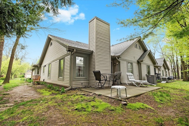 rear view of house with a patio, a chimney, central AC, and a shingled roof