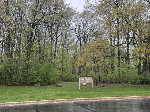 view of green lawn featuring a forest view