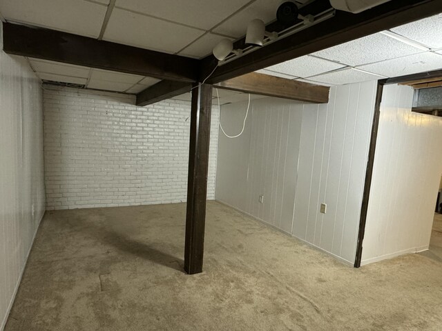 finished below grade area featuring carpet floors, a drop ceiling, and brick wall