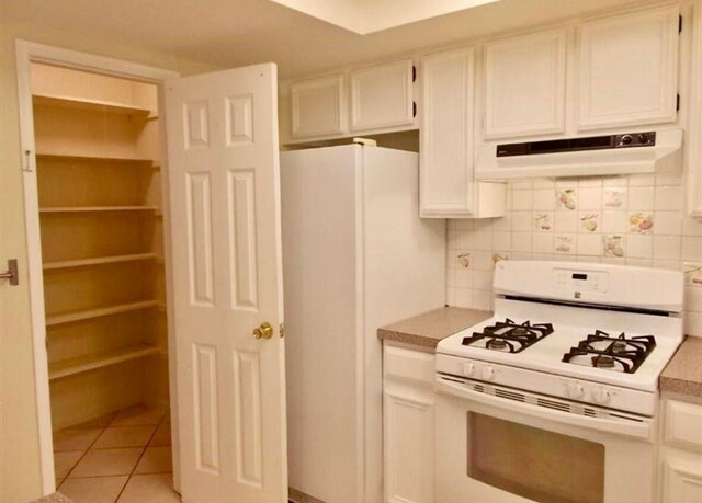 kitchen featuring white appliances, under cabinet range hood, decorative backsplash, light tile patterned floors, and white cabinetry