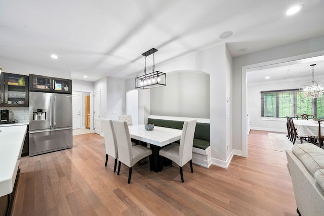 dining space with a chandelier, light wood-style floors, recessed lighting, arched walkways, and baseboards