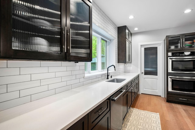 kitchen with a sink, stainless steel appliances, glass insert cabinets, light wood-type flooring, and recessed lighting