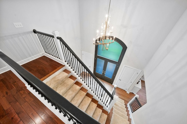staircase with wood finished floors, a chandelier, and a high ceiling