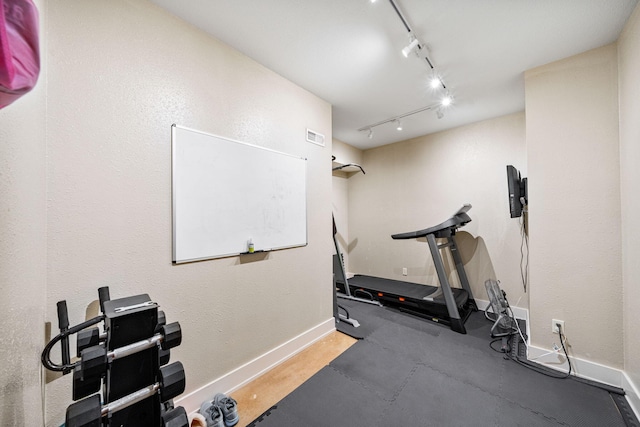 exercise room featuring rail lighting and baseboards