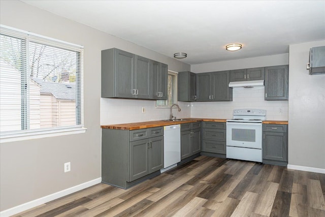 kitchen with white appliances, wood counters, gray cabinetry, under cabinet range hood, and plenty of natural light