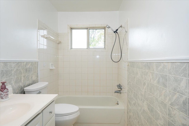 full bathroom featuring tile walls, toilet, vanity,  shower combination, and a wainscoted wall