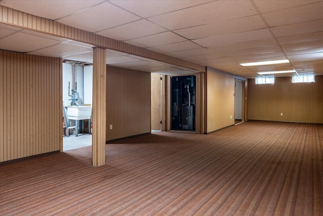 below grade area featuring carpet flooring, a paneled ceiling, wooden walls, and a sink