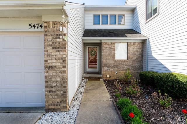doorway to property featuring brick siding, a shingled roof, and an attached garage