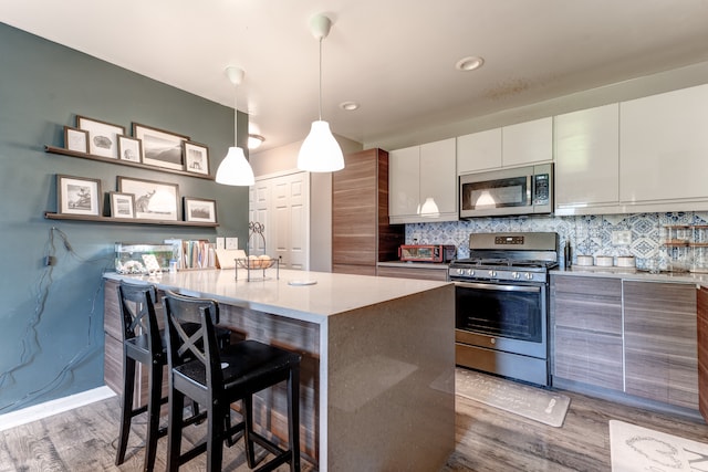 kitchen with stainless steel appliances, wood finished floors, modern cabinets, a kitchen island, and tasteful backsplash