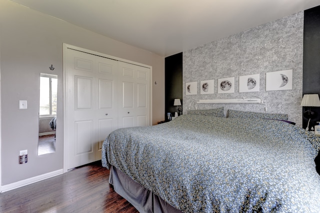bedroom featuring dark wood-style flooring, a closet, an accent wall, and baseboards