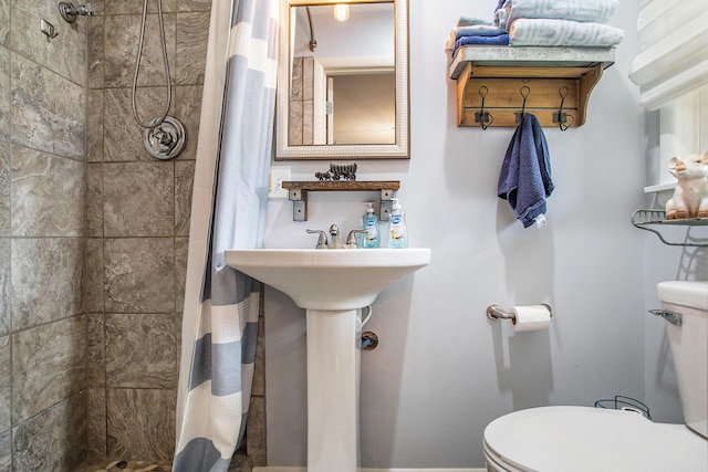 bathroom with toilet, a tile shower, and a sink
