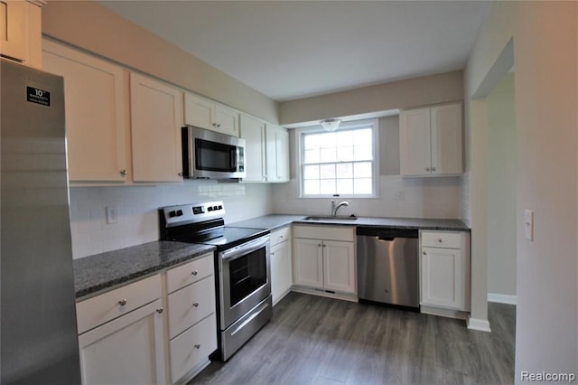 kitchen with appliances with stainless steel finishes, a sink, backsplash, dark wood-style floors, and white cabinetry