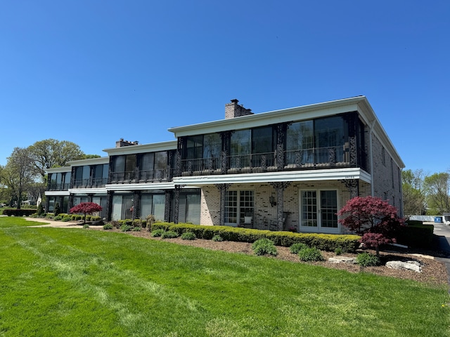 rear view of property with a sunroom, a chimney, brick siding, and a yard