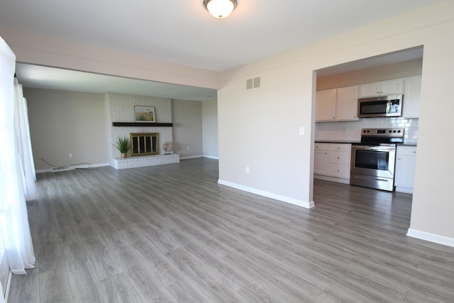 unfurnished living room with baseboards, light wood finished floors, and a brick fireplace