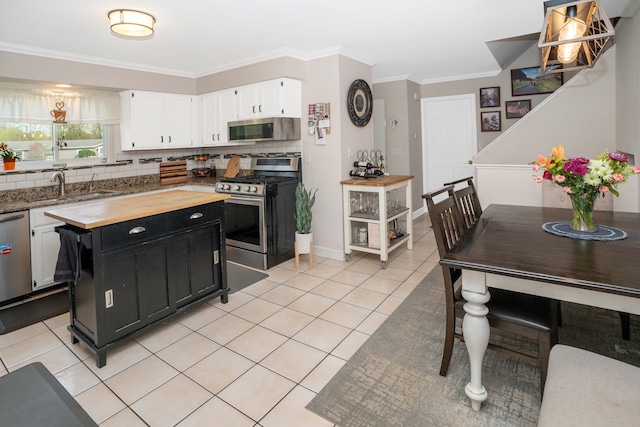 kitchen featuring appliances with stainless steel finishes, wood counters, dark cabinetry, light tile patterned flooring, and crown molding