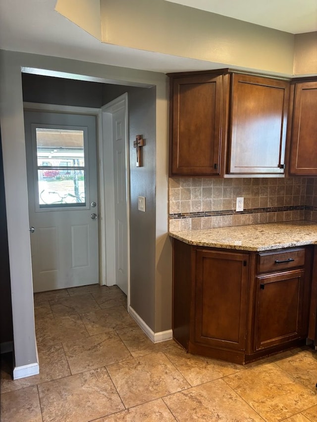 kitchen featuring baseboards, tasteful backsplash, light stone finish flooring, and light stone counters