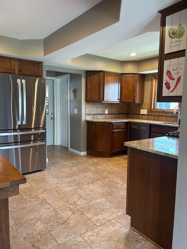 kitchen featuring freestanding refrigerator, a sink, baseboards, light stone counters, and decorative backsplash