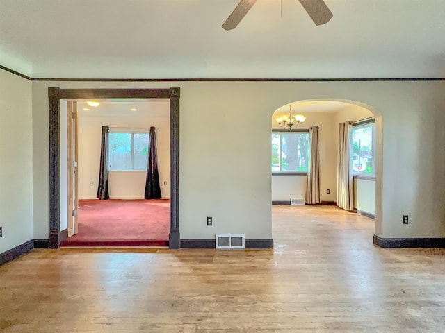 spare room featuring arched walkways, ornamental molding, baseboards, a ceiling fan, and light wood-type flooring