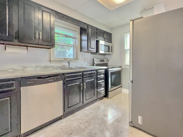 kitchen featuring appliances with stainless steel finishes, dark cabinets, plenty of natural light, a paneled ceiling, and a sink