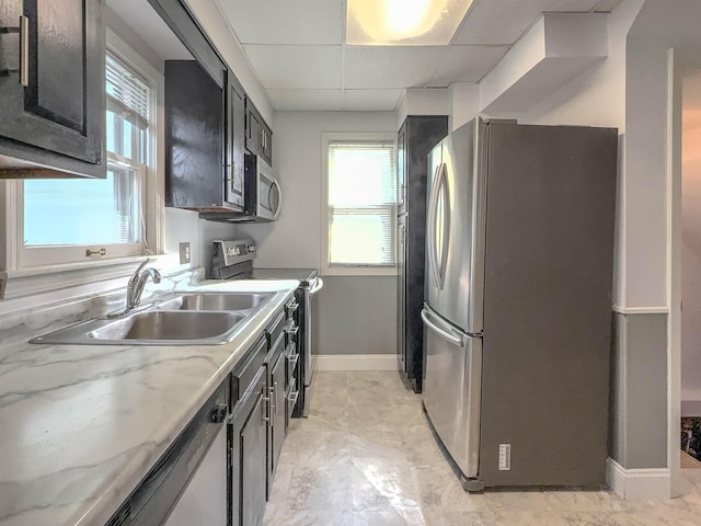kitchen with appliances with stainless steel finishes, baseboards, a sink, a paneled ceiling, and plenty of natural light