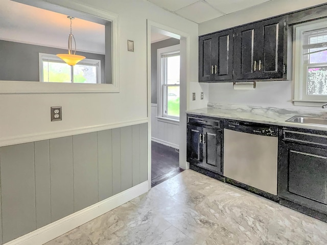 kitchen with dishwasher, dark cabinetry, a wainscoted wall, healthy amount of natural light, and marble finish floors