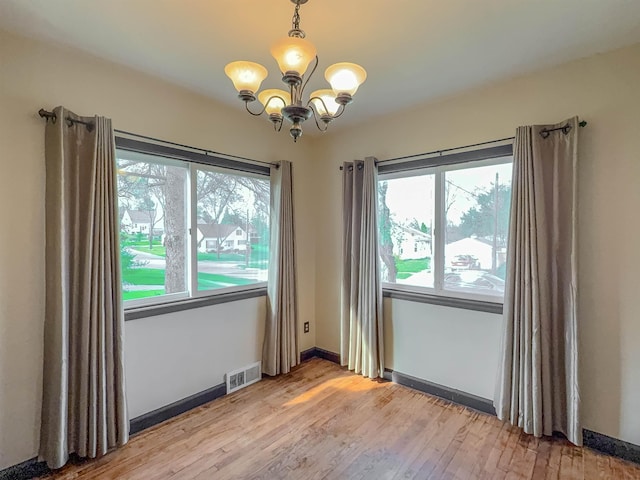unfurnished room featuring a chandelier, healthy amount of natural light, light wood-style floors, and baseboards