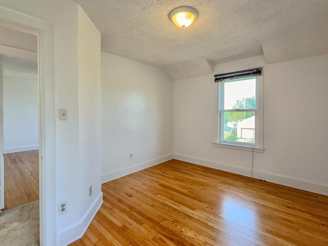 empty room featuring a textured ceiling, light wood-style floors, baseboards, and vaulted ceiling