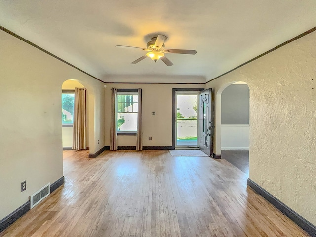 unfurnished room featuring arched walkways, a ceiling fan, a textured wall, wood finished floors, and baseboards