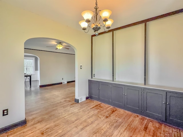 empty room with arched walkways, light wood-style floors, a chandelier, a ceiling fan, and baseboards