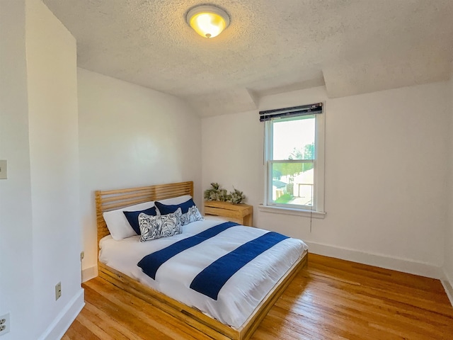 bedroom featuring a textured ceiling, baseboards, and wood finished floors