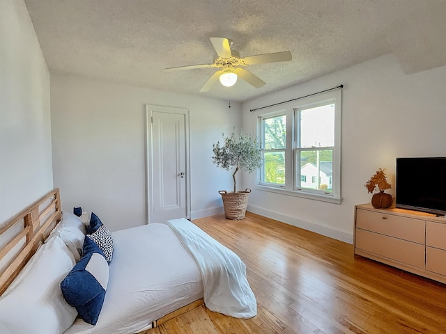 bedroom featuring baseboards, a textured ceiling, light wood-style floors, and a ceiling fan
