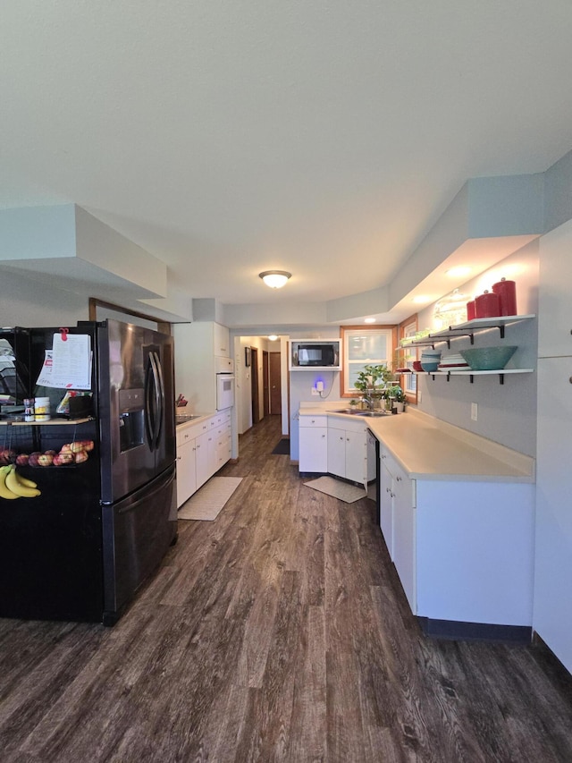 kitchen with refrigerator with ice dispenser, built in microwave, dark wood finished floors, white cabinets, and white oven