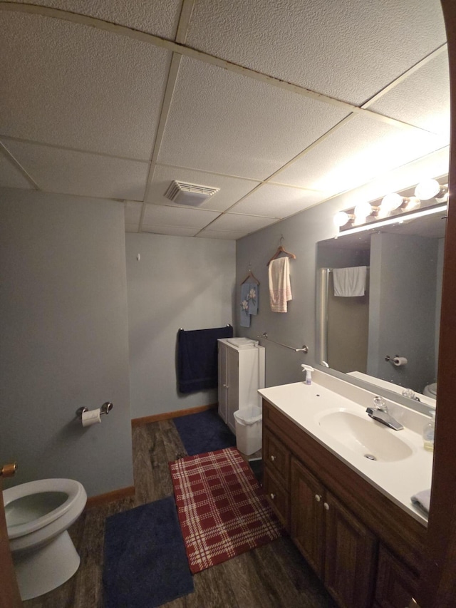 half bathroom featuring toilet, wood finished floors, vanity, a paneled ceiling, and baseboards