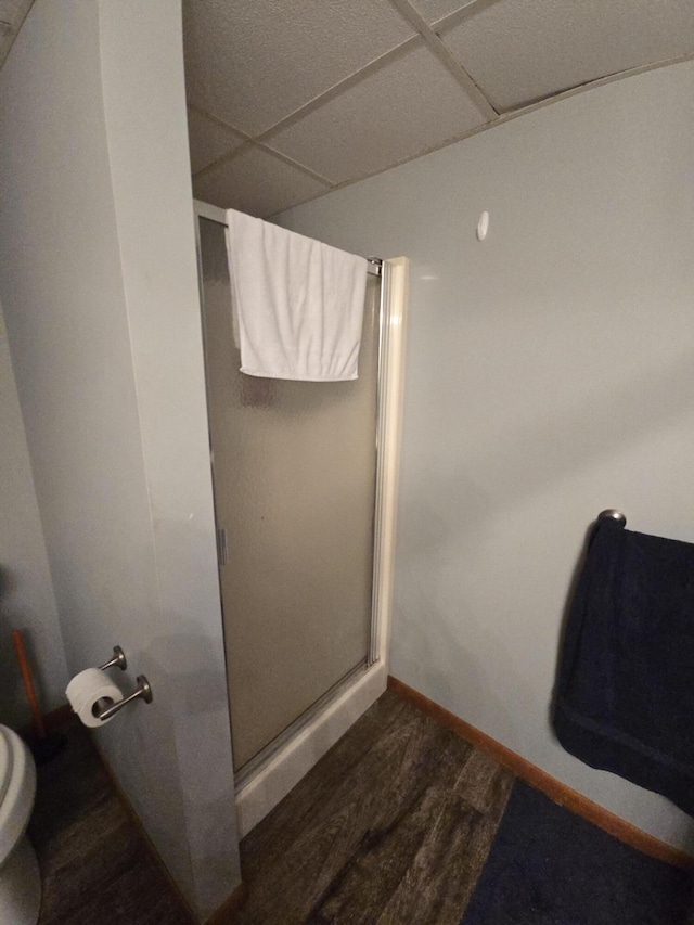 full bath with a paneled ceiling, a stall shower, baseboards, toilet, and wood finished floors