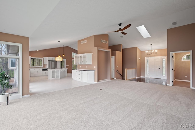 unfurnished living room featuring a skylight, a chandelier, ceiling fan, light carpet, and baseboards